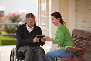 Woman and her husband in a wheelchair in front of their home using a digital tablet