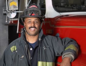 African male firefighter leaning against fire truck